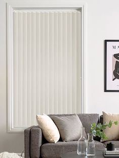 a living room filled with furniture and a window covered in white vertical blind blinds on the wall