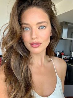 a woman with long brown hair and blue eyes is posing for a photo in the kitchen