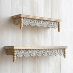 two wooden shelfs with carved designs on them against a white painted wood plank wall