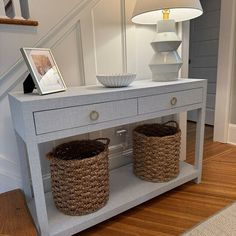 two baskets under a white table with stairs in the background and a lamp on top