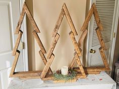 three wooden christmas trees sitting on top of a white mantle next to a candle holder