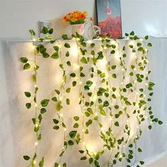 a white curtain with green leaves hanging from it's sides and lights on the side