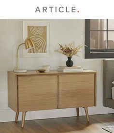 a wooden sideboard with two drawers and a lamp on top in front of a window