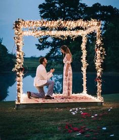 a man and woman kneeling down in front of a gazebo with lights on it