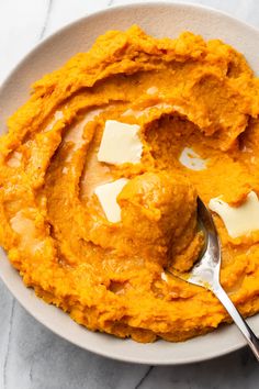 a white bowl filled with mashed sweet potatoes and butter on top of a marble table