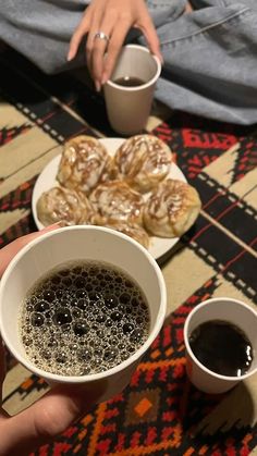 two cups of coffee and pastries on a table with a person holding a plate