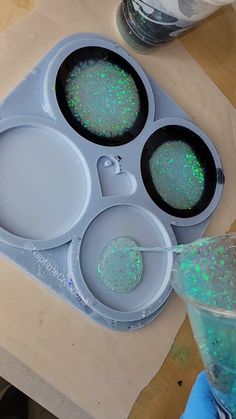 an ice tray with three bowls filled with green liquid and some glitter on the lids