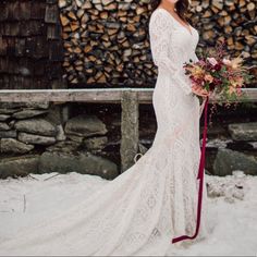 a woman standing in the snow wearing a wedding dress and holding a bridal bouquet