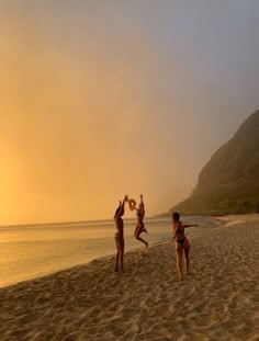 three people jumping up in the air on a beach with mountains and water behind them