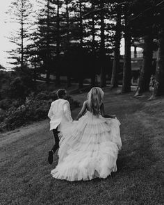 a man and woman walking down a grass covered field next to each other holding hands