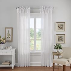 a white chair sitting in front of a window next to a table with flowers on it