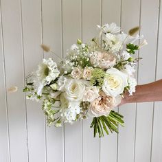 a bouquet of white and pink flowers is held up by someone's hand against a wall