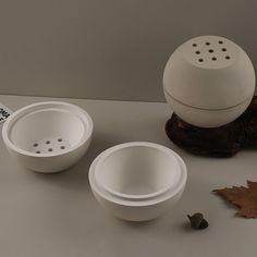 three white bowls sitting on top of a table next to a leaf and a book