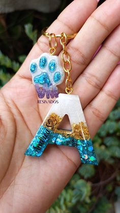 a hand holding a keychain with a dog paw and letter charm on it