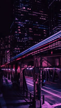 a train traveling over a bridge in the middle of a city at night with lights on