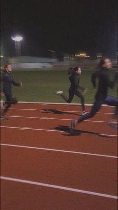 people running on a track at night with lights in the background and one person wearing black