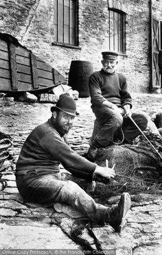 two men sitting on the ground with fishing nets in their hands and one man standing next to them