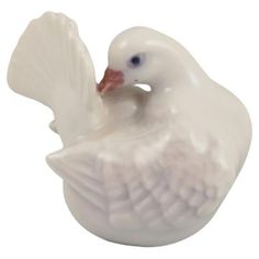 a white ceramic duck with blue eyes and wings on its body, sitting in front of a white background