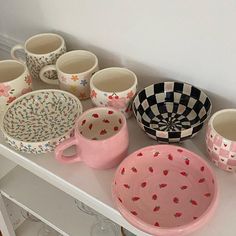 a table topped with lots of cups and bowls on top of a white shelf next to a wall