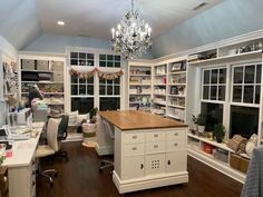 a home office with white cabinets and lots of shelves on the wall, along with a chandelier hanging from the ceiling