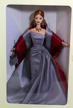 a barbie doll in a box wearing a purple dress and red cape with jewels on it