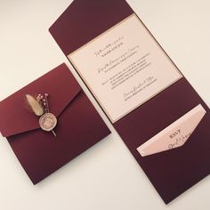 a red and white wedding card with a feather quill on the front is laying next to an envelope