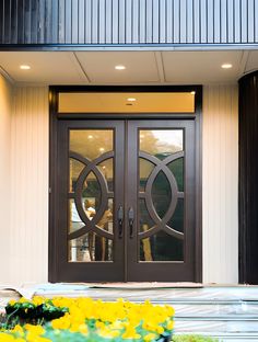 the front entrance to a building with two double doors and yellow flowers on the ground