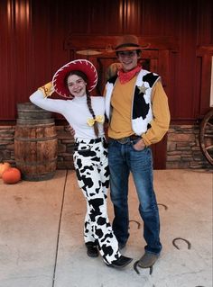 a man and woman dressed up as cows in front of a barn with pumpkins