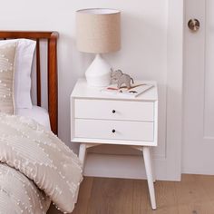 a white nightstand with a lamp on it next to a bed in a small room