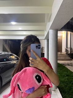 a woman taking a selfie with her cell phone in front of a house and car