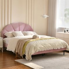 a bed with pink headboard and pillows in a white room next to a window