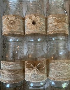 mason jars with burlocks and bows are lined up against a wooden wall, ready to be used as vases