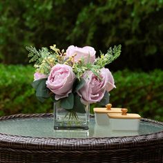 pink roses in a vase on top of a wicker coffee table with greenery