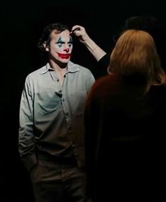 a man with his face painted as the joker is standing next to a woman in a dark room