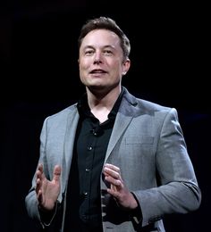 a man standing in front of a black background wearing a gray suit and black shirt