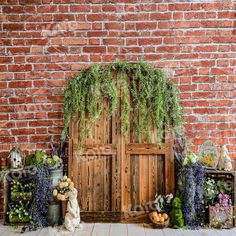 an old wooden door surrounded by plants and other decorations on display in front of a brick wall