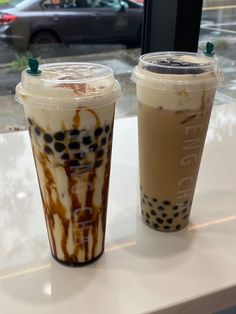 two iced coffees sitting on top of a table next to each other in front of a window