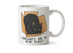 a white coffee mug with a black cat in a box on it's side