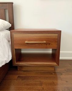 a wooden night stand sitting on top of a hard wood floor next to a bed