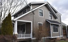 a gray house with white trim and two porches on the second floor is surrounded by trees