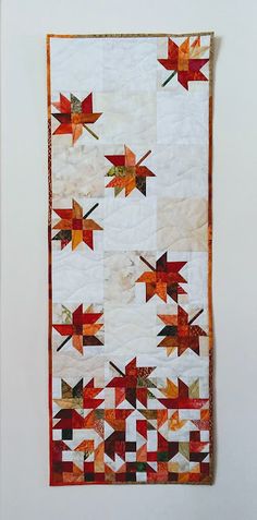 an orange and white quilt with red leaves on it's side, hanging from the wall