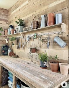 a wooden table topped with lots of pots and pans next to a shelf filled with potted plants