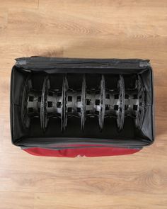 the inside of a black case with wheels in it on a wooden floor next to a red bag