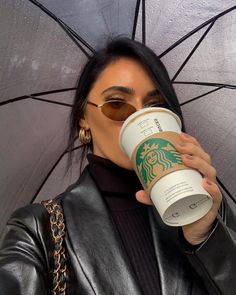 a woman holding up a starbucks cup in front of her face with an umbrella behind her