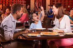 a family sitting at a table eating pizza and drinking wine in a restaurant with red walls