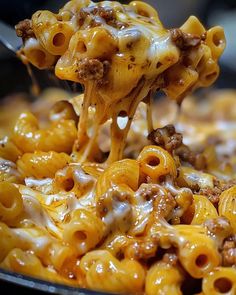 a spoon full of macaroni and cheese being lifted from a skillet with meat