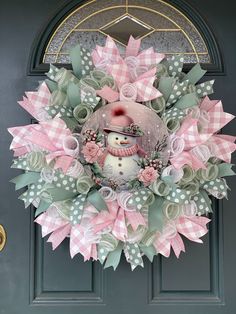 a wreath with a snowman on it hanging from the side of a green door