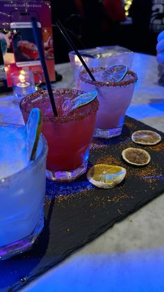 three different types of cocktails on a black tray with blue lights in the background