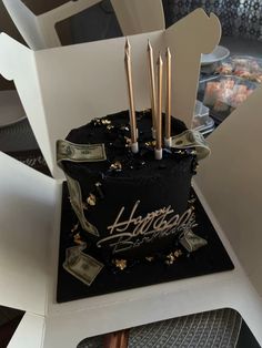 a black and gold birthday cake with dollar bills on the side, sitting in a white chair