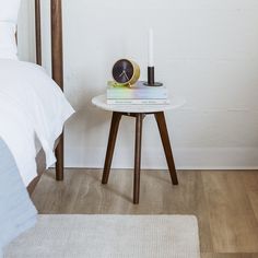 a small table with a clock on it next to a bed